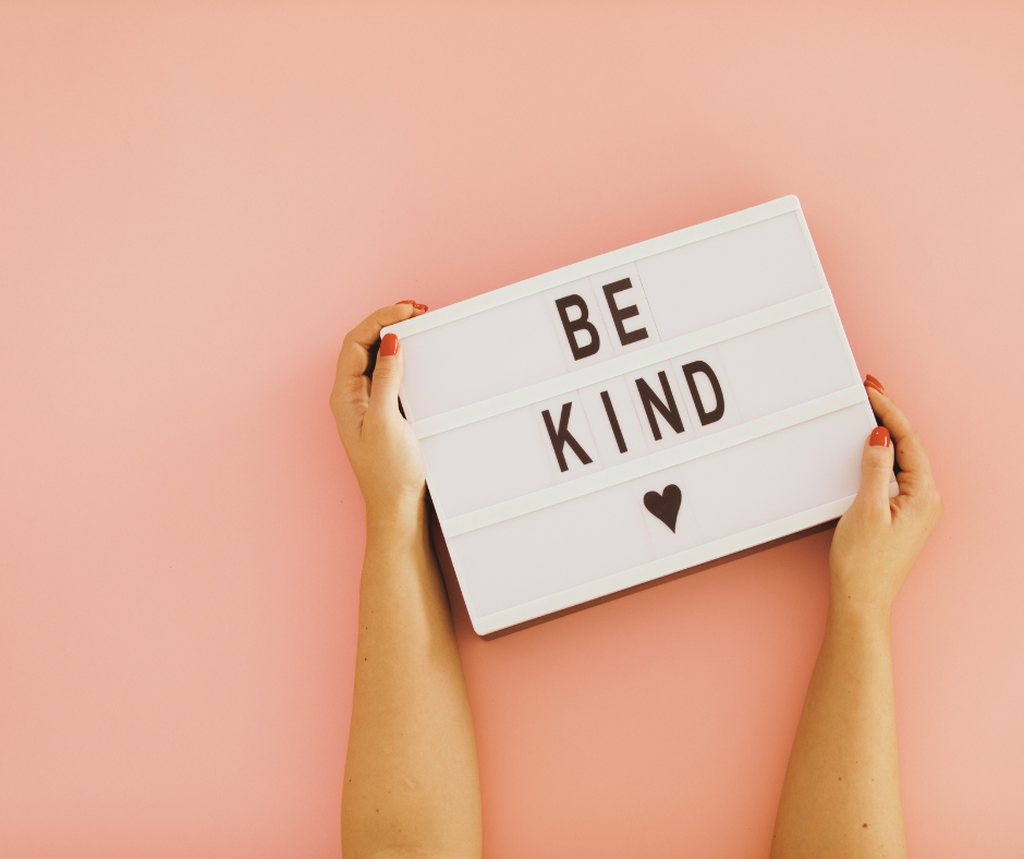 Woman's hand holding a Be Kind sign