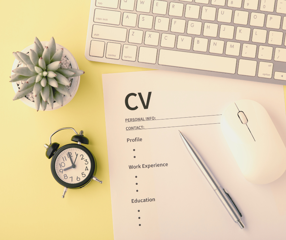 Office desk laid with a succulent plant, clock, keyboard, CV and pen.