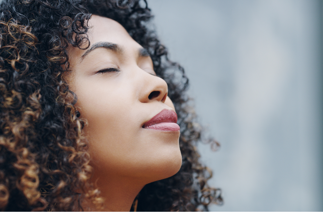 Woman with curly hair breathes deeply with her eyes closed