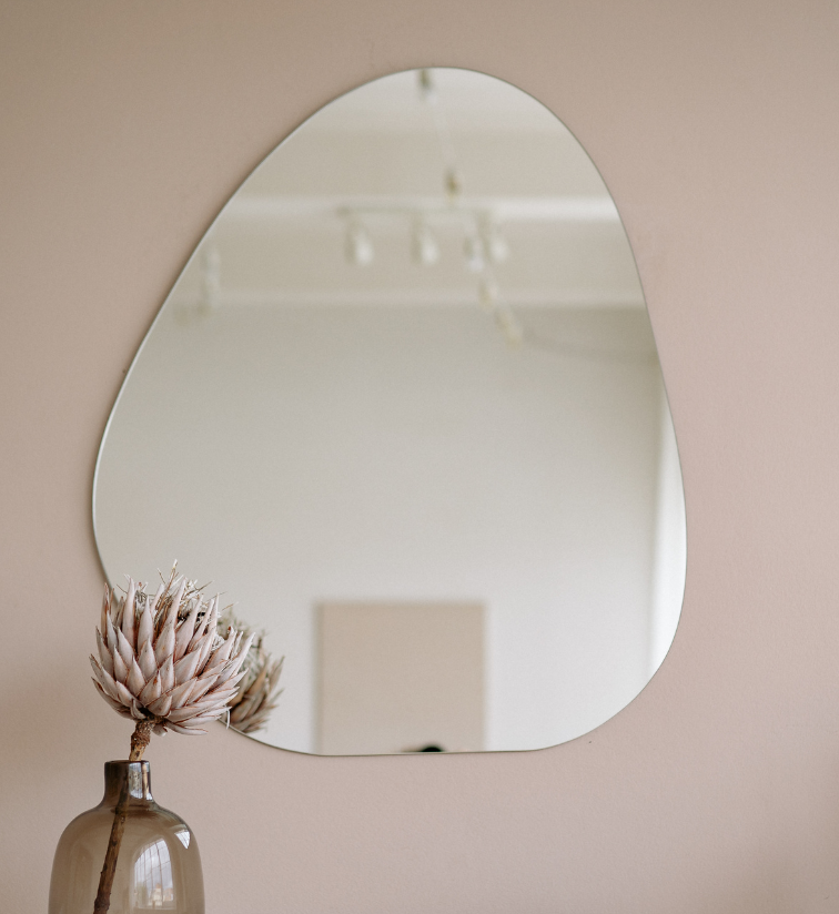 Mirror against a pink wall with ornaments on a sideboard