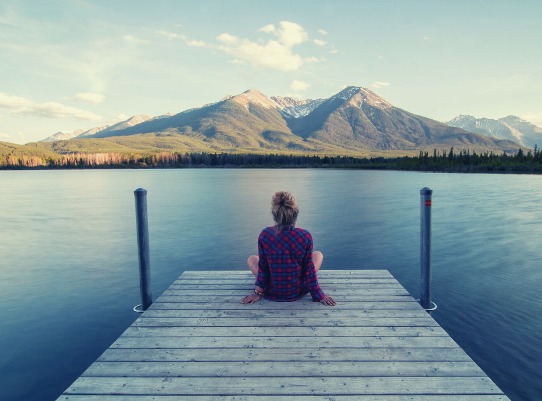 Woman relaxing on a jetty looking out towards two mountains on a summers day