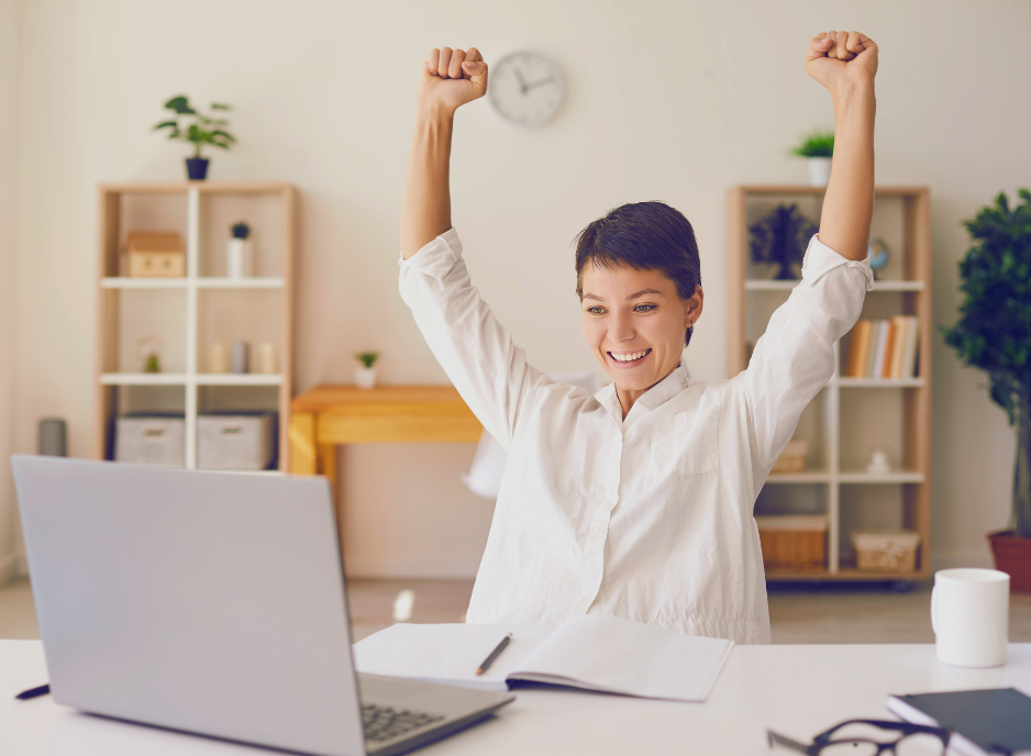 Woman sits triumphant at her desk in front of laptop