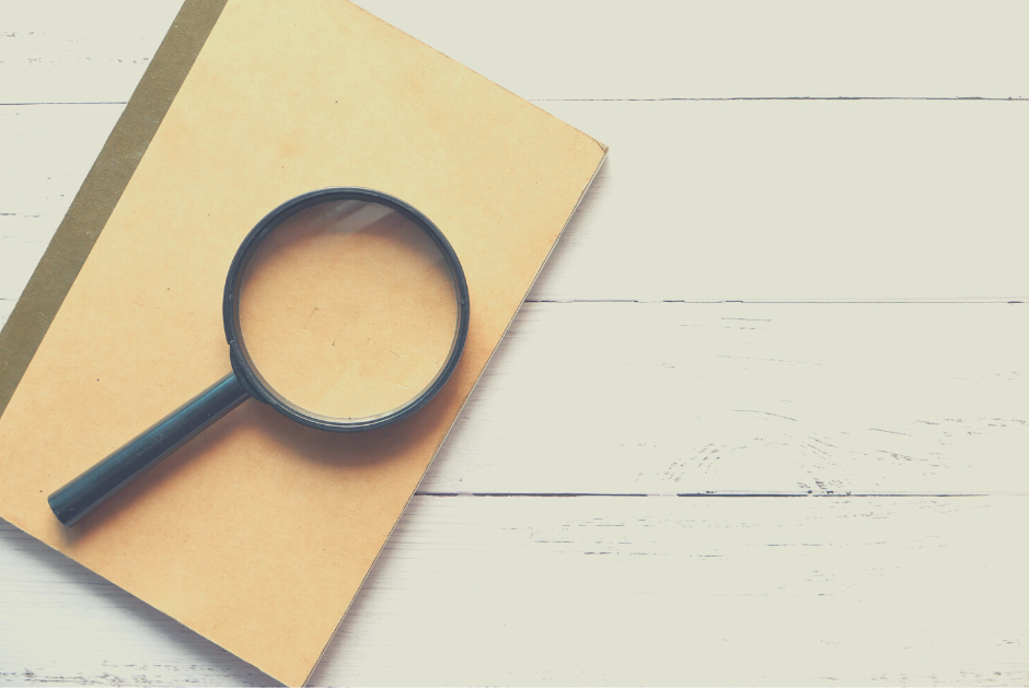 Close up of a black magnifying glass on a brown jotter against a cream wooden floor