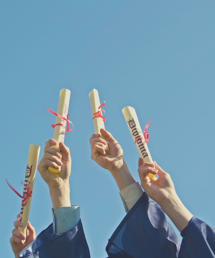 Four arms in blue robes hold up their diplomas on graduation day