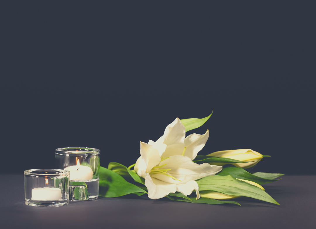 White calla lilies and two white tealight candles against a black backdrop