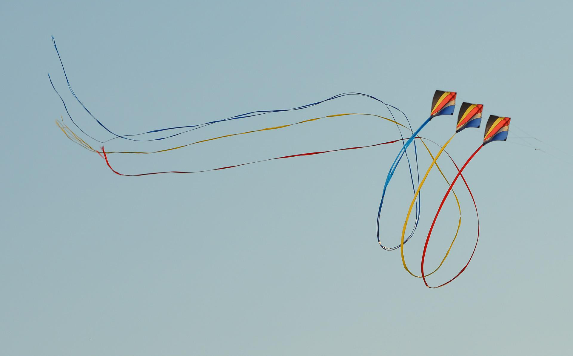 Three multi-coloured kites flying in unison in a blue sky