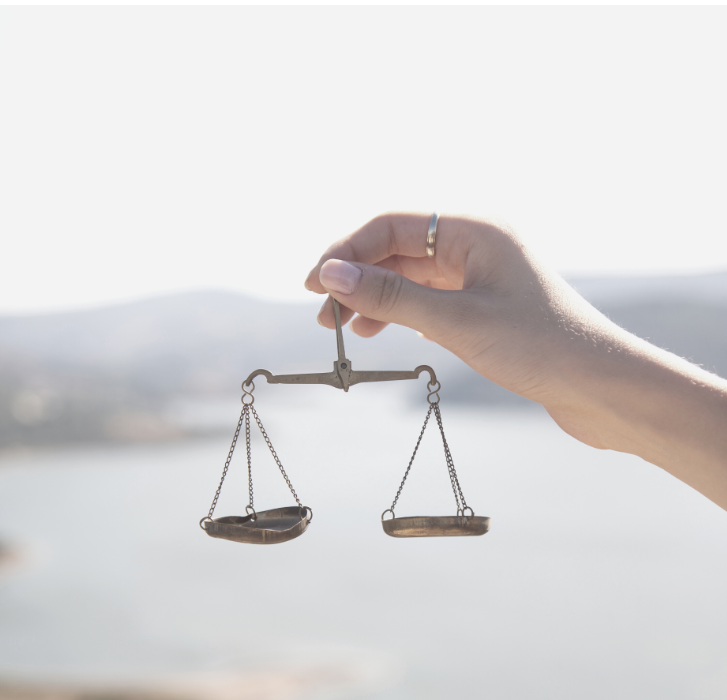 Close up of a woman's hand holding small brass weighing scales against a sunny harbour backdrop