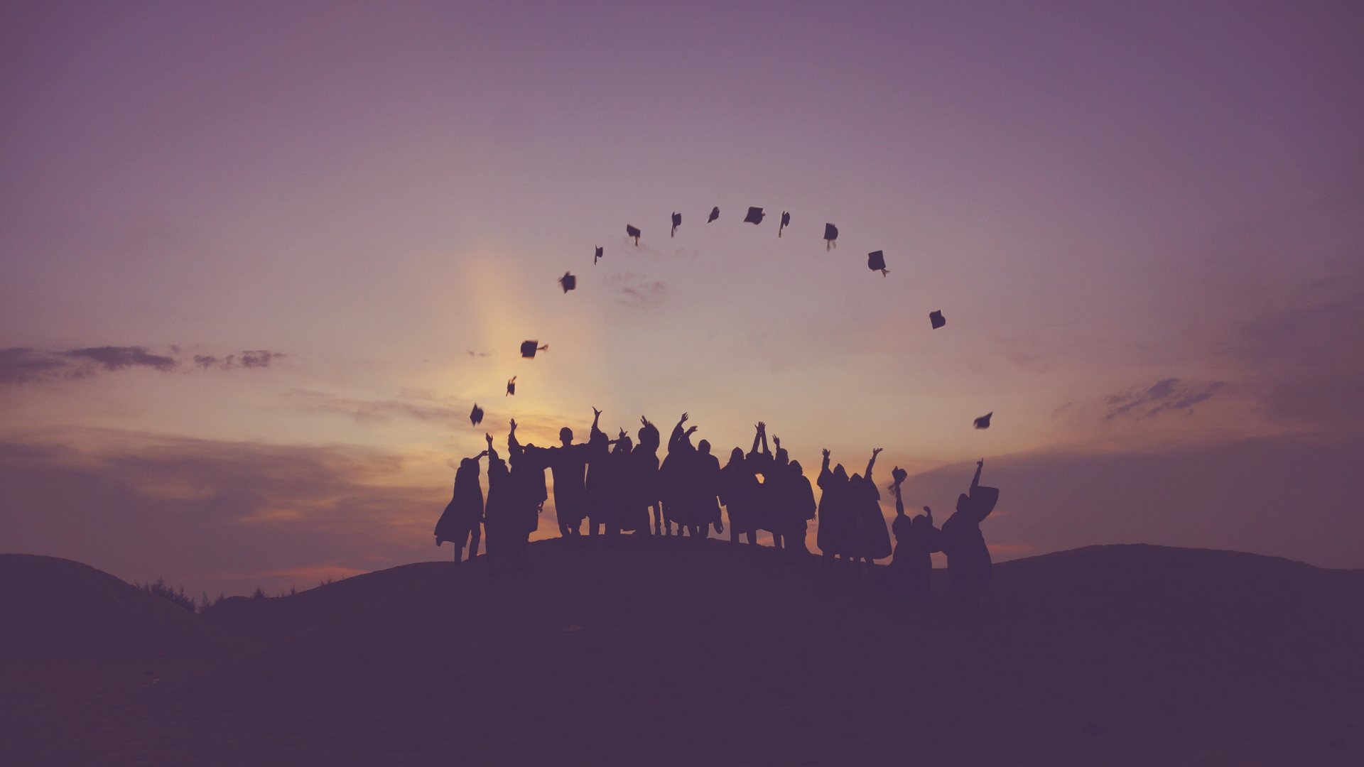 A group of counselling graduates throw their hats in the sky at dusk