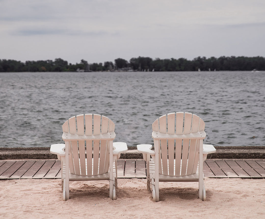 Two white beach chairs on sand overlooking water