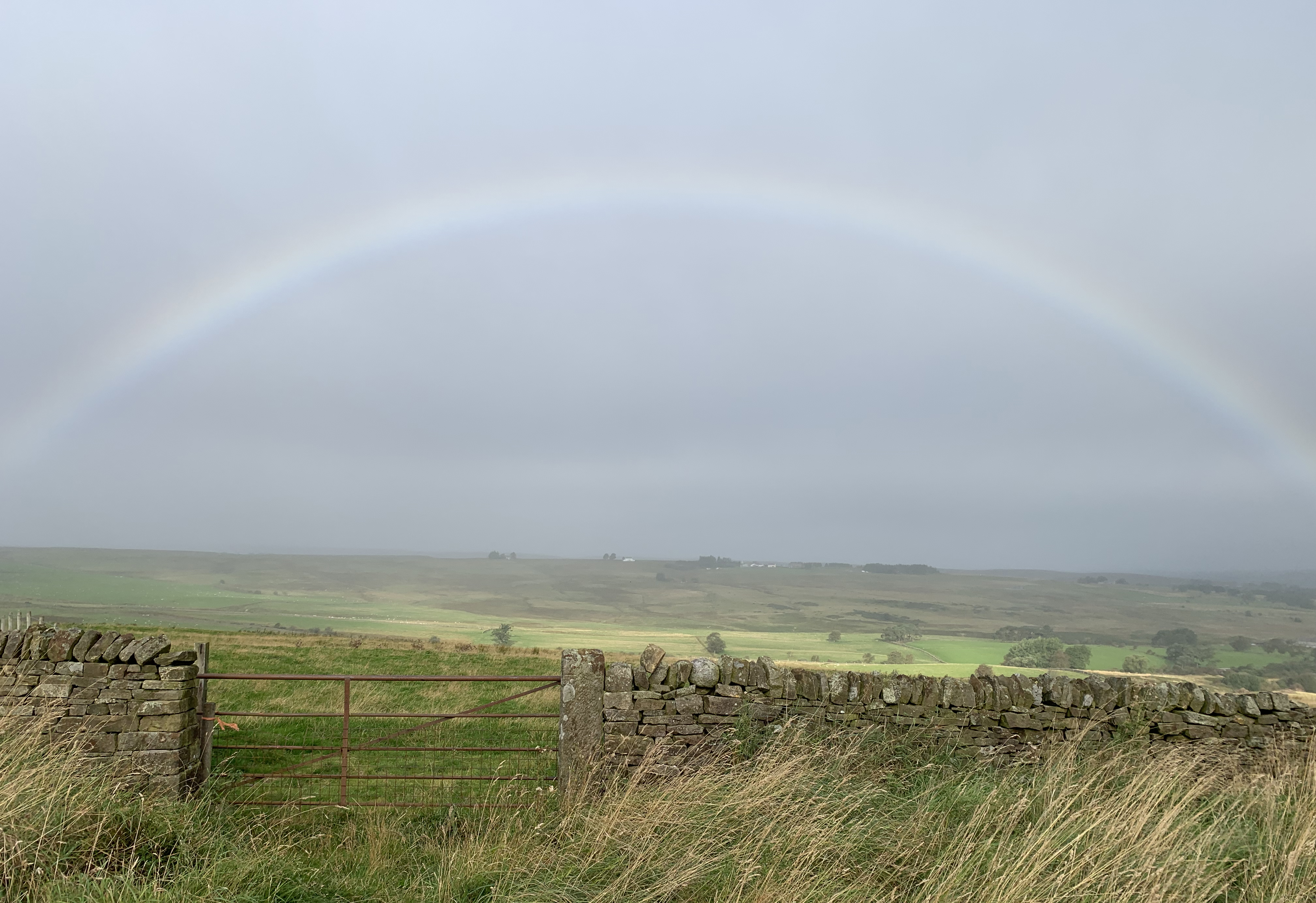Peaceful countryside image showing fields a cloudy sky and a full rainbow.