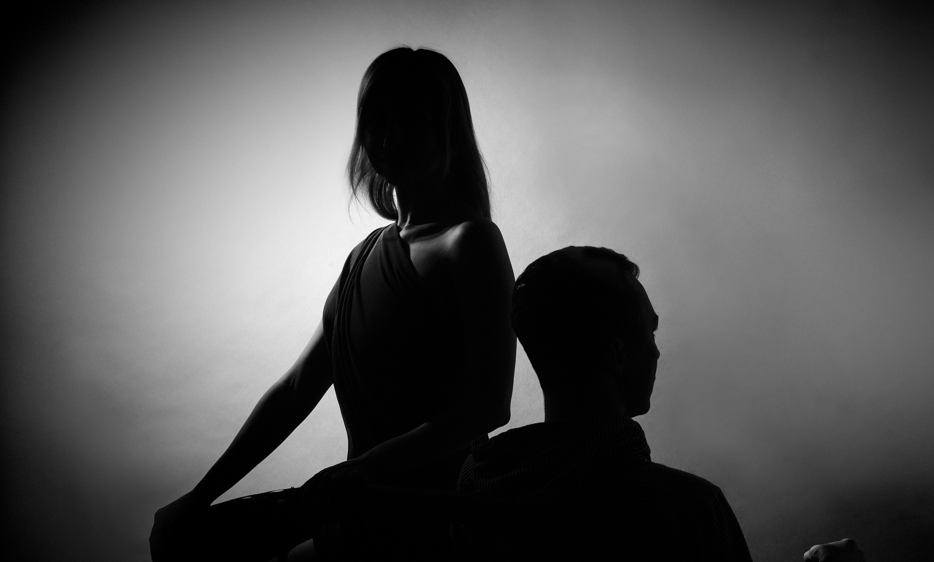 Black and white image showing man and woman turned away from each other in the shadows.
