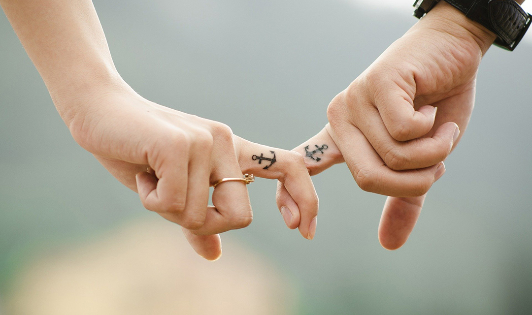 Hands linked at index fingers both with anchor tattoos