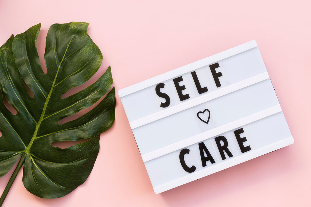 Cheeseplant leaf and white self care sign against a pink background